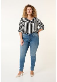Zwart-wit gestreepte blouse met korte mouwen, gecombineerd met lichtblauwe skinny jeans en beige hoge hakken. Eenvoudig ontwerp en getailleerde pasvorm.