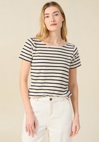 Camiseta de manga corta a rayas en color beige y marino, con escote barco y ajuste relajado. Combinada con pantalones en color crema.