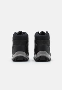 Czarne wysokie buty sportowe z fakturowanym materiałem i gładkimi akcentami syntetycznymi. Gumowa podeszwa z wzorem zapewniającym przyczepność. Widok z tyłu ukazuje wyściełany kołnierz.