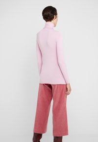 Hellrosa Rollkragenpullover mit langen Ärmeln, kombiniert mit weiten, gerippten Hosen in staubigem Rosé. Glatte Textur mit figurbetonter Silhouette.