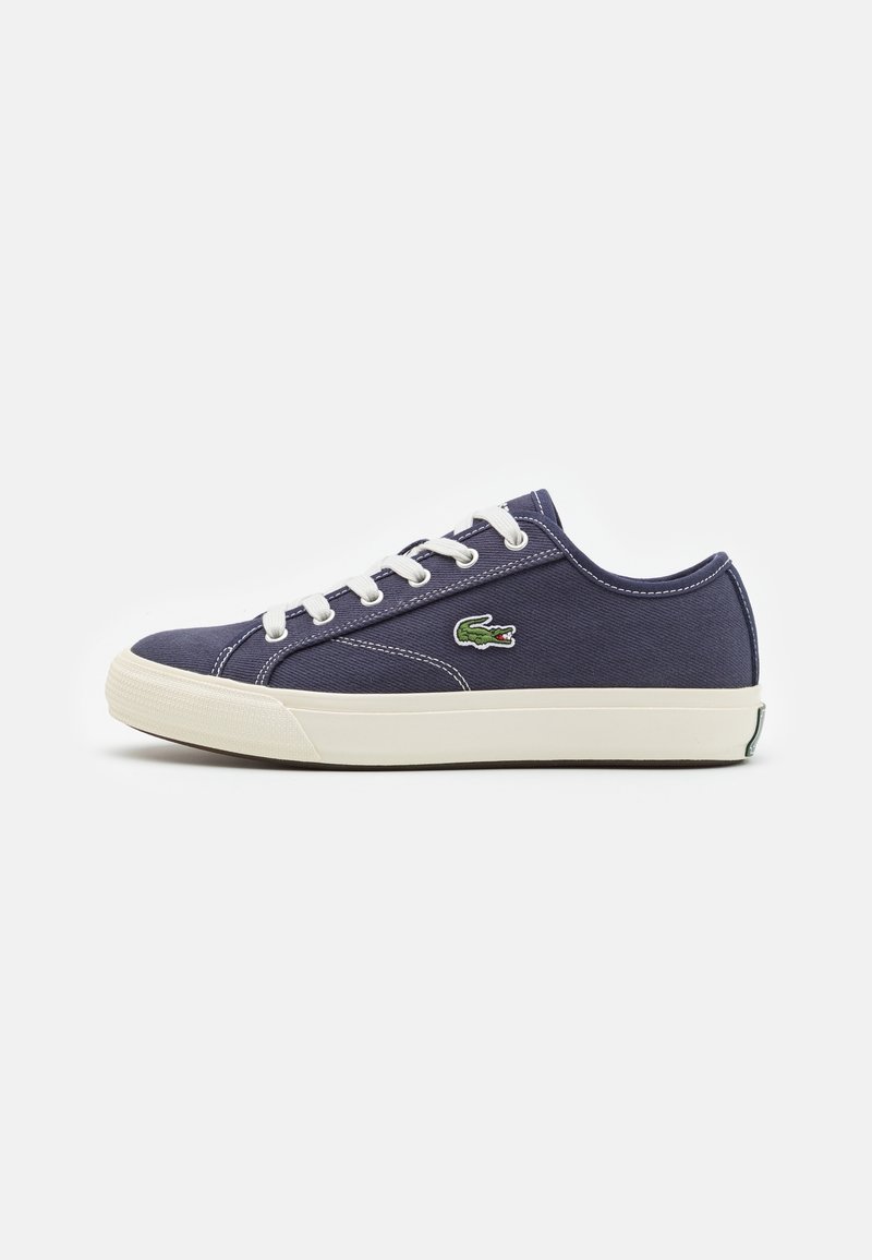 Baskets basses en toile bleu marine avec lacets blancs, semelle en caoutchouc blanche et logo crocodile vert sur le côté.
