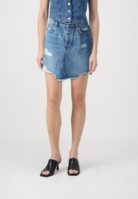 Jeans mini suknja svijetloplave boje s razderanim rubom, koja ima istrošene akcentne detalje i prednje džepove. Uparena s crnim otvorenim sandalama.