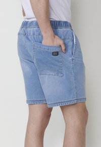 Heledasinised teksapüksid, millel on elastne vöökoht, tagaküljel on tasku ja kontrastsed õmblused. Sile tekstuur.