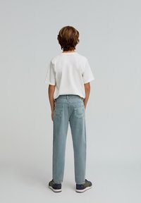 Niño con una camiseta blanca sencilla, jeans rectos azul claro con bolsillos traseros y zapatillas multicolores, visto desde atrás.