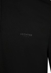 Schwarzes, strukturiertes Poloshirt mit dem geprägten Logo "HECHTER PARIS" auf der linken Seite. Einfaches Design mit klassischem Kragen.