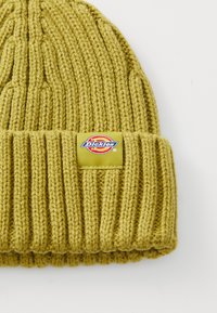 Gul strikket hue med ribbet tekstur og ombuk, forsynet med et rektangulært mærke med "Dickies"-logoet.