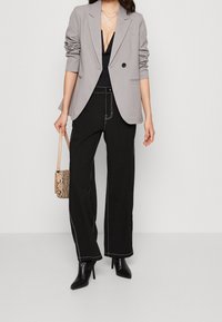 Vala vaaleanharmaa bleiseri, jonka hihat on käännetty, musta paita, leveät mustat housut, joissa on valkoinen ommel, ja mustat korkeat stiletto-kengät. Pieni käärmeennahkakuosiset käsilaukku.