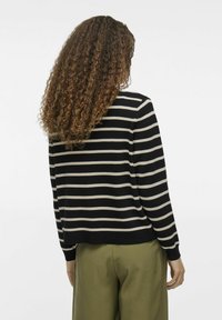 Joslota džemperis melnā un gaiši brūnā krāsā, ar apaļu kakla izgriezumu, garām piedurknēm un brīvu piegriezumu, apvienots ar olīvzaļiem biksēm.