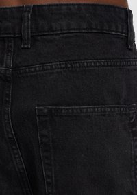 Jeans de mezclilla negra con una cintura alta, bolsillos estándar y un acabado limpio en las costuras, que ofrecen una superficie ligeramente texturizada.