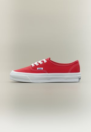 Červené nízké plátěné tenisky Vans s bílými tkaničkami a silnou bílou gumovou podešví na neutrálním pozadí.