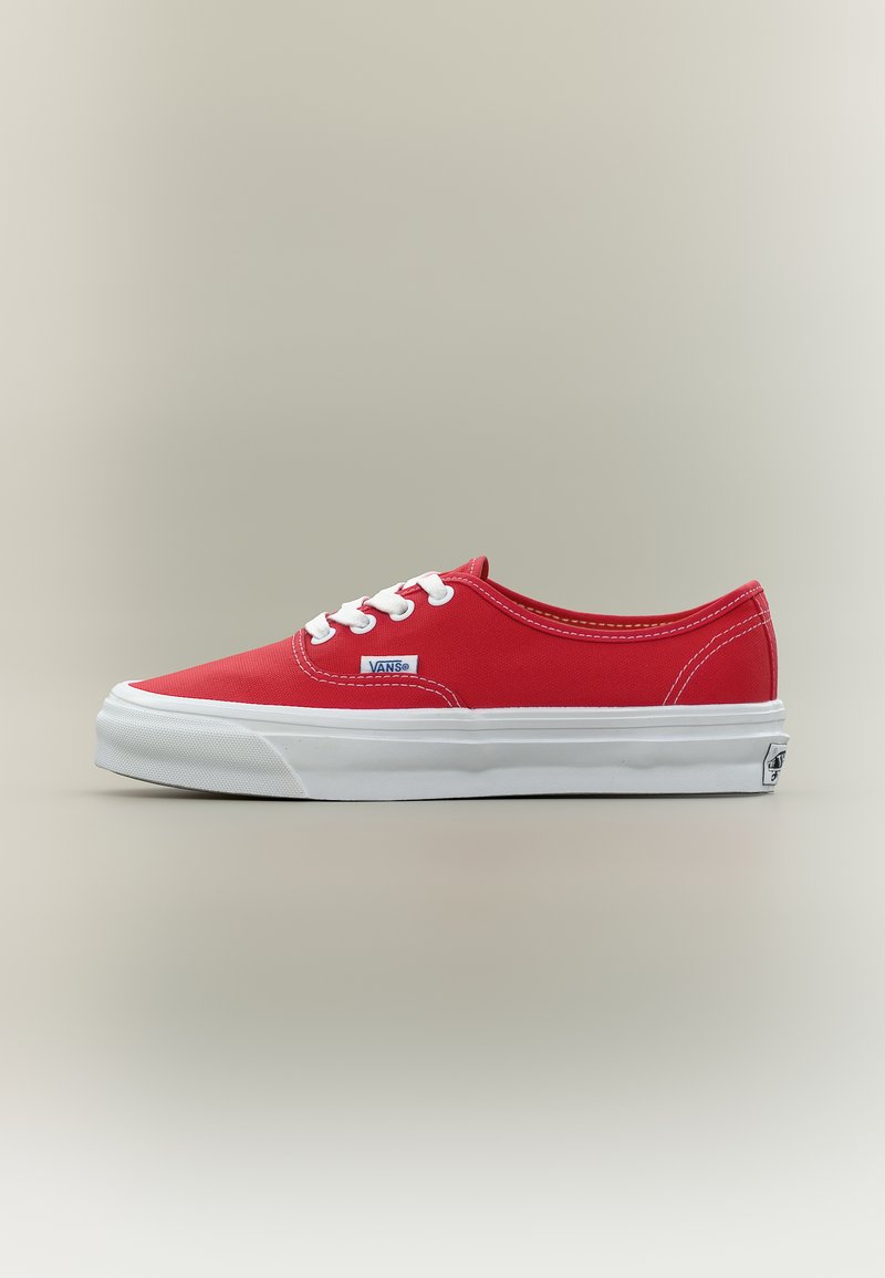 Κόκκινο απλό πάνινο παπούτσι Vans χαμηλού προφίλ με λευκά κορδόνια και χοντρή λευκή ελαστική σόλα σε ουδέτερο φόντο.