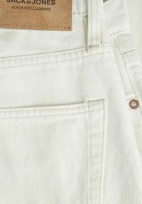 Tessuto di denim chiaro con una trama a coste diagonali, caratterizzato da un'etichetta in pelle con la dicitura "JACK & JONES" e un dettaglio sulla tasca anteriore.