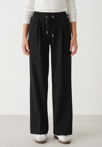 Zwarte wijd uitlopende broeken gemaakt van zachte stof, met een elastische tailleband met trekkoord en zilverkleurige hardware-accenten.