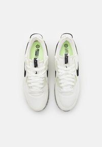 Ein Paar weiße Sportschuhe mit schwarzen Swoosh-Logos, weißen Schnürsenkeln und neongrünen Innensohlen, von oben auf einem weißen Hintergrund betrachtet.