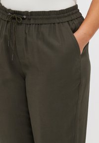 Pantalones ligeros y verdes con cintura elástica y cordón ajustable. Cuenta con bolsillos laterales y una textura suave.