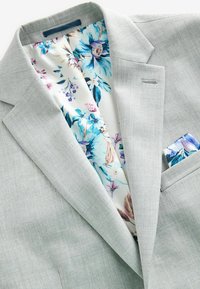 Blazer gris claro con forro interior de patrón floral en azul, rosa y blanco. Incluye un pañuelo de bolsillo con diseño floral a juego.