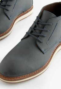 Zapatos de cuero gris con acentos azules, diseño de cordones, punta redonda, superficie texturizada y suela de goma color crema con costuras marrones.