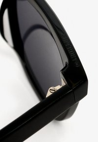 Zwarte zonnebril met een glanzende afwerking, voorzien van donker getinte glazen, een minimalistisch rechthoekig ontwerp en een zilveren scharnier met merkdetail.