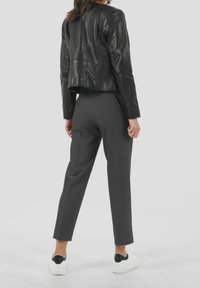 Černá křácená kožená bunda s vertikálními švy, doplněná o šedé elegantní kalhoty a bílé tenisky s černými detaily.