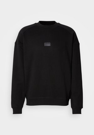 Black sweatshirt featuring a round neck, raglan sleeves, and a glossy black logo patch at the chest. Soft material with a relaxed fit.