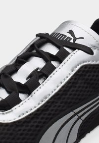 Κοντινό πλάνο μαύρου και ασημένιου αθλητικού παπουτσιού Puma με μαύρα κορδόνια και λογότυπο Puma στη γλώσσα και στο πλευρό.