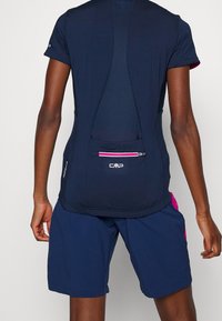 Persona con pantalones cortos deportivos azul marino y una camiseta de manga corta azul marino con un panel de malla y un bolsillo trasero con cremallera.