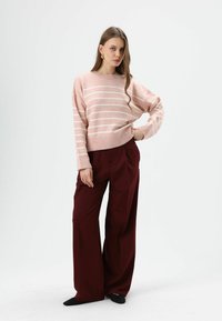 Hellrosa gestreifter Pullover mit geripptem Saum und Bündchen, kombiniert mit weiten bordeauxroten Hosen. Das Outfit zeichnet sich durch eine entspannte Passform und glatte Texturen aus.