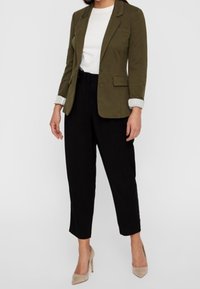 Olivgrön skräddarsydd kavaj, vit t-shirt med rund hals, svarta tapered byxor och beiga klackskor. Kavajen har en spetsig krage och knappstängning.