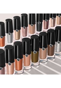 Des flacons de vernis à ongles dans diverses nuances, y compris orange, argent et marron, avec un capuchon noir brillant et un logo circulaire, ainsi qu'une base transparente.