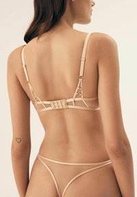 Beżowy zestaw bielizny o przejrzystym wzornictwie, z regulowanymi ramiączkami i złotymi detalami. Posiada zapięcie na haczyk z tyłu oraz minimalne zakrycie.