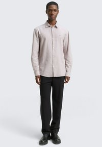 Lichtroze blouse met een klassieke kraag, lange mouwen en een subtiele textuur, gecombineerd met zwarte broek en stevige zwarte schoenen.