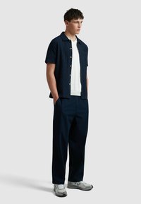 Donker marineblauwe kortarmshirt met een gestructureerd patroon, gecombineerd met losse donkere broek en lichtgekleurde sneakers.