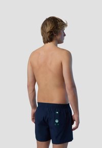 Shorts da bagno blu con vita elastica, dotati di una tasca posteriore con accessori verdi e dettagli accentuati. Materiale liscio e leggero.