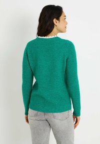 Suéter verde de punto con acabado texturizado, mangas largas y dobladillo acanalado. Presenta un cuello blanco con borde ondulado visible en la parte trasera.