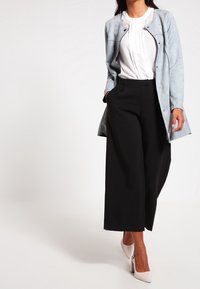 Chaqueta azul claro, abotonada, con acentos negros, usada sobre una blusa blanca y pantalones de pierna ancha negros. Modelo lleva unos tacones claros.