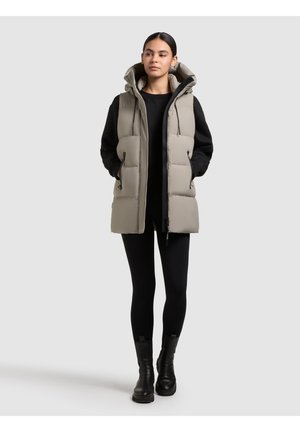 Leichte graue gepolsterte Weste mit Kapuze, Reißverschluss vorne und zwei Seitentaschen. Kombiniert mit einem schwarzen Langarmoberteil und schwarzen Leggings.