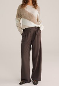 Pull rayé beige et marron avec une texture duveteuse sur un côté, associé à un pantalon marron taille haute à jambes larges. Ballerines noires avec des clous.