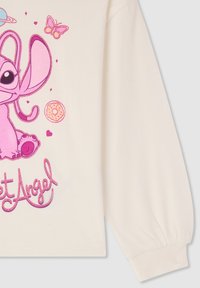 Felpa color crema con un personaggio dei cartoni animati rosa, dotato di grandi orecchie, circondato da cuori, farfalle e una grafica di un donut. Maniche lunghe.