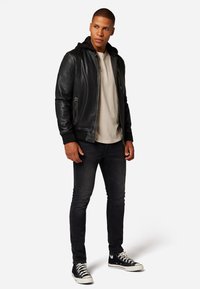 Svart läderbomberjacka med ribbade manschetter, en grå t-shirt, mörka slim-fit jeans och svarta högskoor med vita sulor.