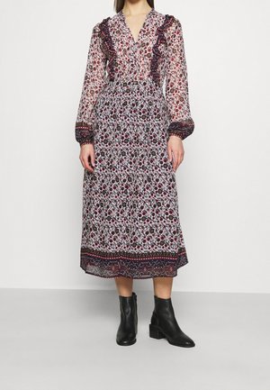 Robe longue transparente à fleurs avec col et poignets à volants. Fond blanc à imprimé floral multicolore, portée avec des bottines noires jusqu'à la cheville.