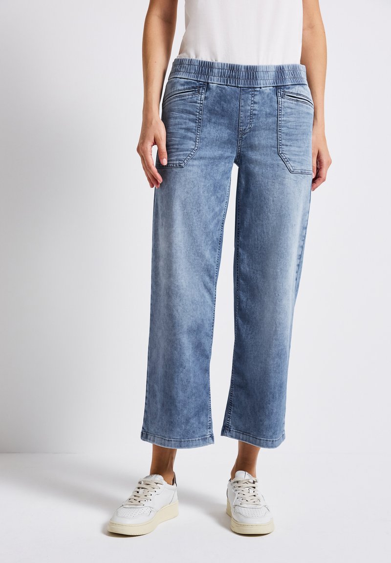 Pantalons culottes en denim bleu clair avec une taille élastique, poches avant et coupe décontractée, associés à des baskets blanches.