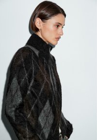 Maglione di lana in motivo argyle khaki e nero con colletto alto, dotato di chiusura con zip e un aspetto texturizzato e soffice.