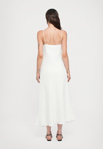 Vestido blanco sin mangas con tirantes finos, espalda recta y falda fluida. Fabricado en material ligero con una textura suave.