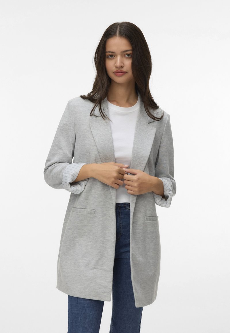 Jasnoszary blezer, teksturowany materiał, otwarty przód, dwie przednie kieszenie, podwinięte mankiety odsłaniające paskowane wykończenie, noszony na białej koszulce i niebieskich dżinsach.