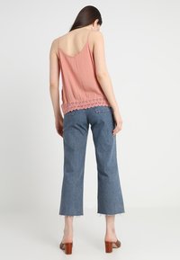 Top in colore pesca con bordo in pizzo, abbinato a jeans di denim blu a vita alta con orlo sfrangiato. Sandali con tacco a blocco marroni.