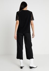 Svart topp med spetsärmar, kombinerad med svarta vida byxor och vita ankelboots. Toppen har en rund halslinje och en slät textur.