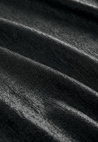Tessuto nero con una superficie morbida e pelosa e una leggera lucentezza. Presenta pieghe ondulate e dettagli intricati.