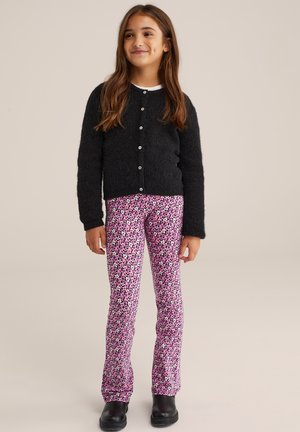 Cárdigan negro de pelaje con botones frontales, combinado con leggings florales rosas que presentan pequeñas flores blancas y verdes. Botines negros completan el atuendo.