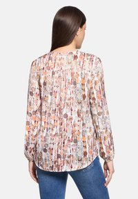 Langarmshirt aus leichtem Stoff mit einem mehrfarbigen kreisförmigen Muster. Der Rücken hat Falten, und der Saum ist leicht gewellt.