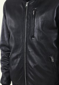 Zwarte leren bomberjack met een gestructureerde afwerking, voorkant met rits, en twee zijzakken, inclusief een kleine ritszak op de borst.